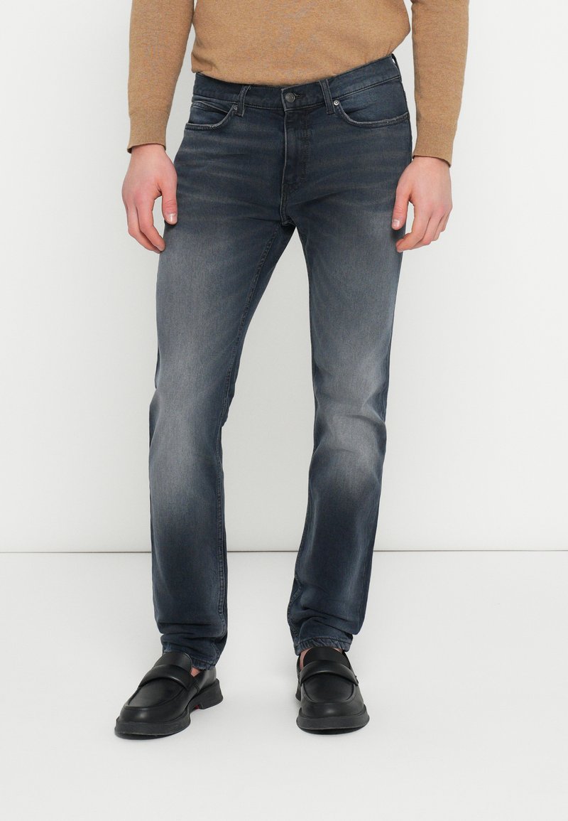 Blugi din denim albastru închis, croială slim, cu cinci buzunare, ușor decolorați și cu fermoar și nasture la brâu. Asortați cu pantofi negri.