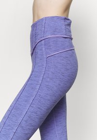 Högmidjade leggings i en melerad lila tyg, med kontrasterande sömdetaljer och en slät yta.