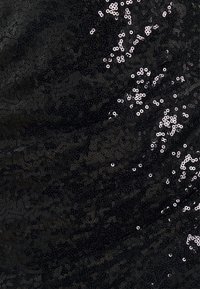 Svart tyg som är täckt av glänsande paljetter, vilket skapar ett texturerat utseende med en reflekterande kvalitet. Paljetterna varierar i storlek och inriktning.