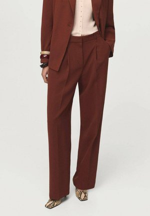 Rust-colored tailored trousers with a high waist, sharp creases, and a loose fit, paired with patterned ankle boots.