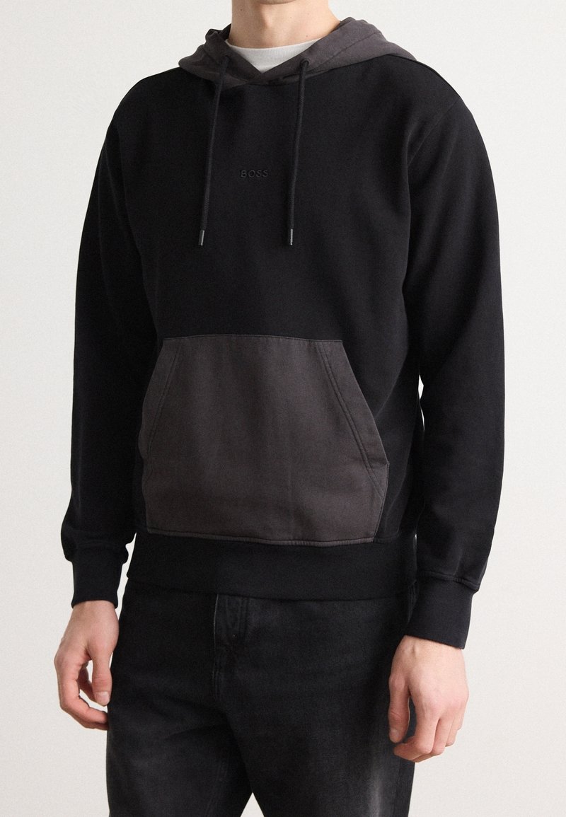 Sudadera de algodón negra con un bolsillo frontal gris, cordones y un logo sutil en el pecho. Presenta puños y dobladillo acanalados.