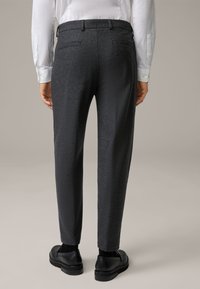 Pantaloni grigi scuri su misura con tessuto testurizzato,fit snello e tasche posteriori, abbinati a scarpe nere e dettagli sottili.