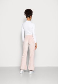 Vit långärmad topp med en åtsittande design, i kombination med ljusrosa utsvängda byxor med ett subtilt mönster, fulländat med vita sneakers.