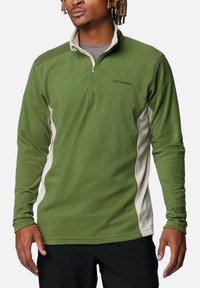 Pullover in pile verde con collo a zip a un quarto, caratterizzato da pannelli laterali color crema e un piccolo logo sul petto. Tessuto morbido, maniche lunghe.