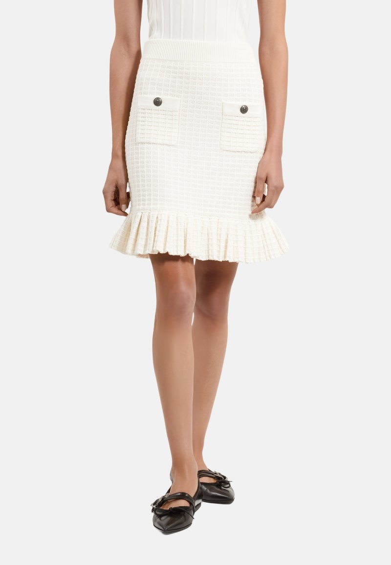 Jupe blanche texturée avec une bordure évasée, dotée de deux poches avant à rabat avec des accents de boutons. Ceinture côtelée pour un look ajusté.