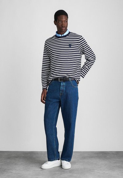Navy and white striped long-sleeve shirt with crew neck, paired with blue denim jeans and white sneakers. Black belt accents the outfit.