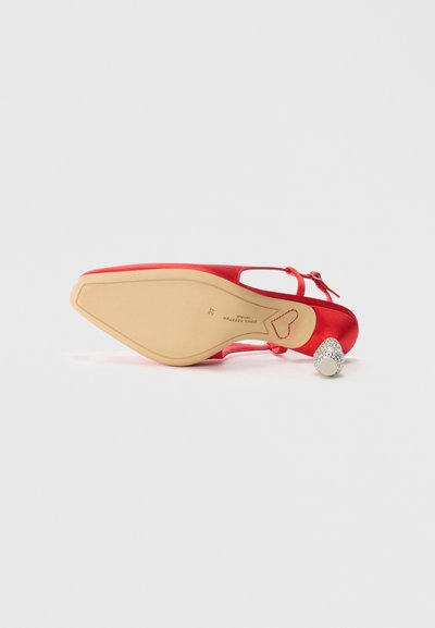 Red satin high-heeled shoe with a pointed toe, ankle strap, smooth texture, and a round, sparkly silver heel accent.