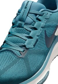 Chaussures de sport teal avec tige en mesh, système de laçage texturé et semelle rembourrée avec le logo "Zoom" sur le côté.