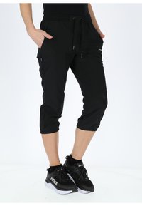 Pantaloni neri cropped realizzati in materiale leggero, dotati di una cintura elastica, due tasche laterali e un design slim fit. Abbinati a scarpe da ginnastica nere.