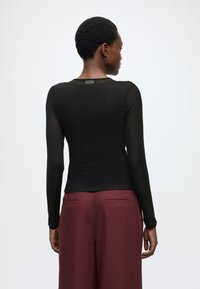 Μαύρο μακρυμάνικο τοπ από διαφανές ύφασμα, εφαρμοστή σχεδίαση με στρογγυλή λαιμόκοψη. Συνδυάζεται με μπορντό ψηλόμεσο παντελόνι.