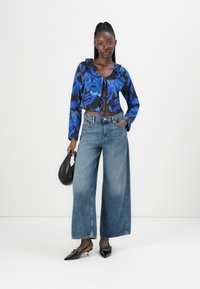 Blusa floreale blu e nera a maniche corte, jeans in denim chiaro a vita alta e gamba larga, borsa nera e décolleté nere appuntite. Texture morbide.