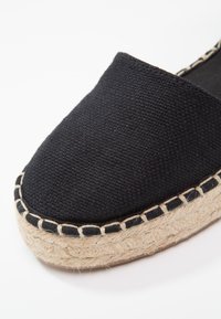 Espadrille en toile noire avec une semelle en corde de jute, dotée d'un bord cousu et d'un dessus texturé pour plus de durabilité et de confort.