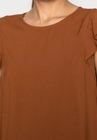 Top marrón de manga corta con cuello redondeado y detalle de mangas con volantes, confeccionado en una tela suave y ligera.