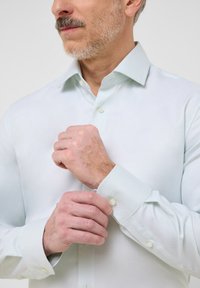 Camicia azzurro chiaro a maniche lunghe realizzata in tessuto testurizzato, con un collo classico e dettagli con bottoni sui polsini, che offre un aspetto ordinato e curato.