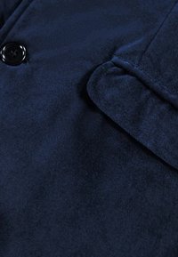 Camicia di tessuto blu navy con una trama morbida, dotata di un singolo bottone nero e una tasca a pattina sul lato sinistro.