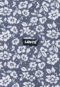 Tela con estampado floral en azul marino y blanco, que presenta una trama texturada similar a un gofre. Incluye un parche con el logo negro de Levi's.