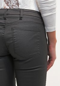 Pantalones de imitación cuero grises con un diseño ajustado, que cuentan con un bolsillo trasero y una textura suave. La cinta de la cintura incluye detalles de costura.