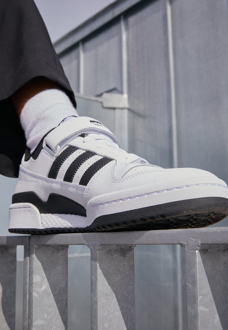 Hvide sneakers med sorte detaljer, med en glat læderoverdel, tre-stribe design, polstret krave og struktureret gummisål.
