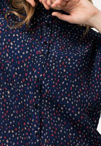Navy blue button-up shirt with a soft texture, featuring a speckled pattern in red, beige, and blue. Black buttons detail the front.