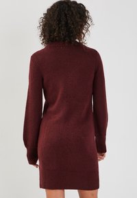Bordowa dzianinowa sukienka z długimi rękawami, wysokim kołnierzem oraz prążkowanymi mankietami i dołem. Teksturowana tkanina o miękkim wyglądzie.