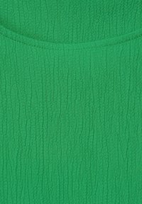 Grön texturerad tyg med ett skrynklat mönster. Ytan har en lätt lyster och visar subtila variationer i färg och djup.