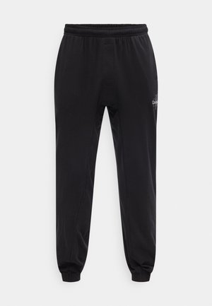 Pantalon de jogging noir avec taille et poignets élastiques, petit logo blanc sur la partie supérieure de la cuisse, présenté sur un fond blanc uni.