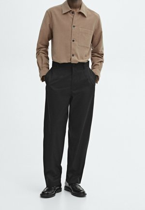 Beżowa koszula sztruksowa na guziki z kieszenią na piersi, zestawiona z czarnymi spodniami z wysokim stanem i czarnymi skórzanymi butami. Minimalistyczny design, gładka faktura.