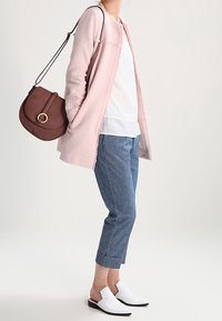 Cardigan texturé rose clair, haut à couches blanc, pantalon en denim bleu cropped, et chaussures blanches à enfiler. Sac bandoulière marron avec quincaillerie dorée.