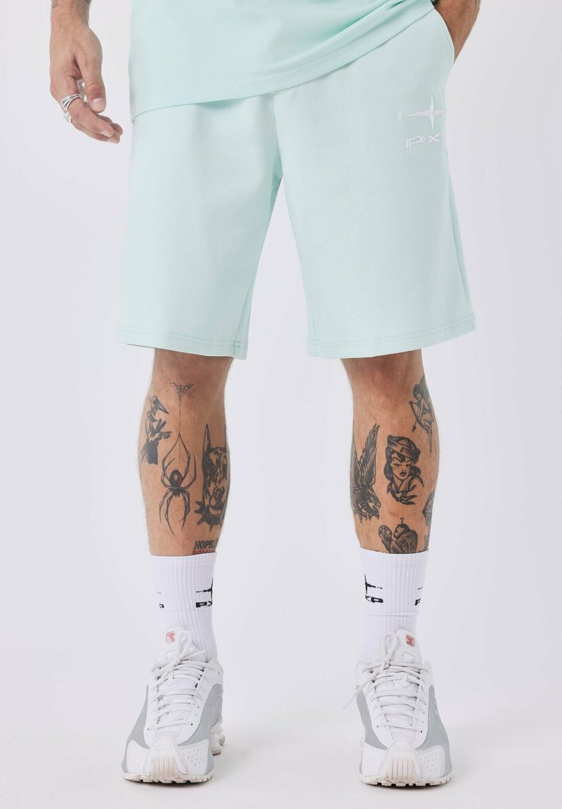 Shorts bleu-vert clair avec une coupe décontractée, dotés de poches latérales et d'un logo brodé. Portés avec des chaussettes blanches et des chaussures de sport grises et blanches.