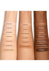 Muestras de tonos crema y marrón claro en brazos, etiquetadas con nombres y códigos para cada color, mostrando varios tonos de piel y matices.