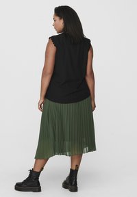 Fekete ujjatlan felső fodros vállrészsel, amelyet egy plisszírozott zöld midi szoknyával és fekete fűzős bokacsizmával párosítanak.