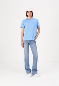 Light blue cotton t-shirt with short sleeves, paired with light blue flared jeans and white sneakers. The model also wears a pink cap.