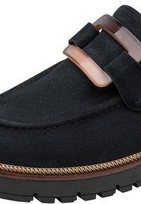 Mocassin en daim noir avec semelle épaisse, boucle décorative marron transparente et bordure tressée beige au-dessus de la semelle sur fond blanc.
