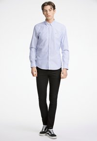 Camicia in cotone a righe azzurre e bianche con colletto button-down, indossata con pantaloni slim-fit neri e sneakers nere con lacci bianchi.