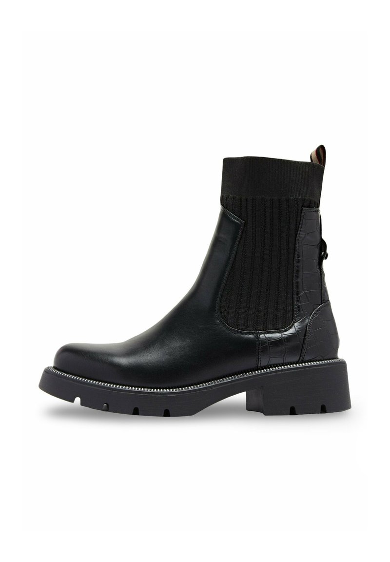 Bottine noire en cuir et textile élastique. Dotée d'un motif croco texturé, d'une semelle épaisse et d'un accent métallique décoratif.