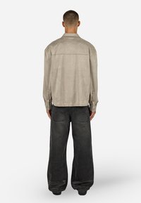 Bézs velúr ing gombos záródással és egyenes szabással, laza szabású sötétszürke farmernadrággal, hátoldali zsebfekvéssel párosítva.