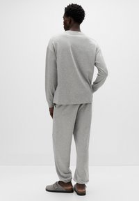 Szary dres z bluzy i spodni dresowych, miękka tkanina, luźny krój, elastyczne mankiety, w zestawie z szarymi wsuwanymi butami ozdobionymi klamrą.