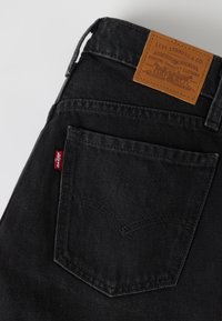 Poche arrière d'un jean en denim noir avec une étiquette rouge Levi's et un patch en cuir marron Levi Strauss & Co au-dessus de la poche.