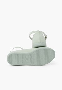 Zapatos verde menta con una textura suave, una correa en el tobillo y una suela de goma con patrón. Claramente marcado "Hecho en España."
