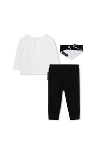 Witte lange mouwen shirt met een knoop aan de achterkant, zwarte leggings en een zwart-wit bandana met knoopdetail. Zachte stof, gladde textuur.