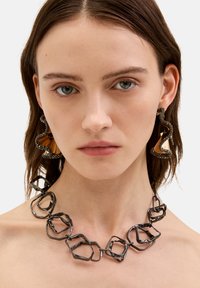 Sort metal halskæde med uregelm�æssige sekskantede led. Store abstrakte øreringe har et struktureret mørkt ydre lag og en glat guldaccent.