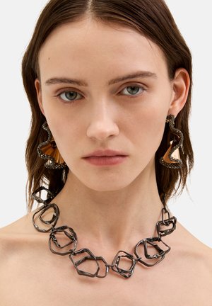 Czarny naszyjnik z metalu z nieregularnymi sześciokątnymi ogniwami. Duże abstrakcyjne kolczyki z teksturowaną ciemną warstwą zewnętrzną i gładkim złotym akcentem.