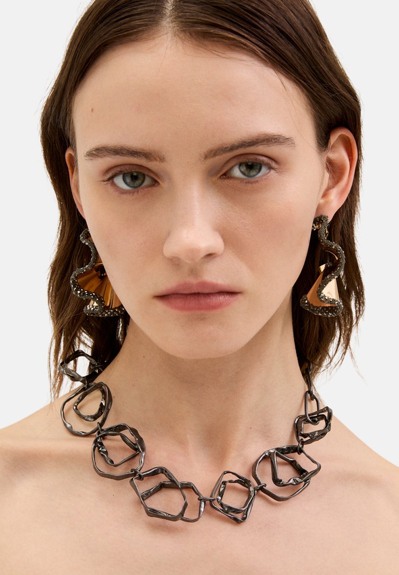 Sort metal halskæde med uregelmæssige sekskantede led. Store abstrakte øreringe har et struktureret mørkt ydre lag og en glat guldaccent.