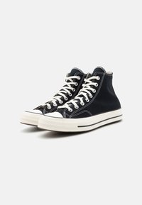 Høye sneakers laget av svart lerret med hvite lisser, gummitåhette og teksturerte såler. Har kontrastsømmer og logopreg.