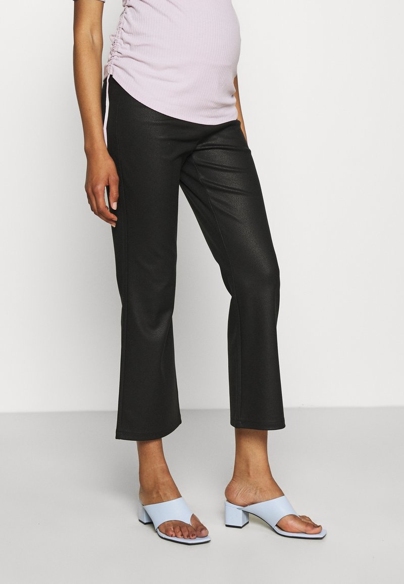 Persona che indossa pantaloni neri a vita alta, una maglia violacea arricciata chiara e mule a tacco blocco aperte di colore blu chiaro su uno sfondo neutro.