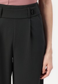 Pantalons noirs ajustés avec une texture lisse, dotés d'une fermeture à bouton et de plis sur le devant. La taille est soigneusement finie avec des passants de ceinture.