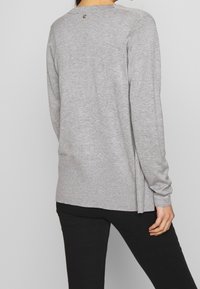 Maglione grigio a maglia con collo rotondo, maniche lunghe e orlo a coste. Presenta un piccolo emblema decorativo nella parte posteriore del collo.