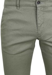 Close-up van olijfgroene broek met zicht op de tailleband, knop, riemlus en de naad van de voorkzak.