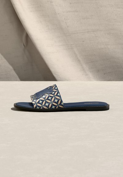 Πλατφόρμα σανδαλιών με μπλε σόλα και φαρδιά υφασμάτινη λουρά με μπλε και μπεζ γεωμετρικό μοτίβο, σε ουδέτερο φόντο.