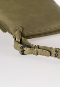 Pochette in pelle verde oliva con texture liscia, dotata di chiusura con zip e tracolla removibile fissata da una fibbia nera.